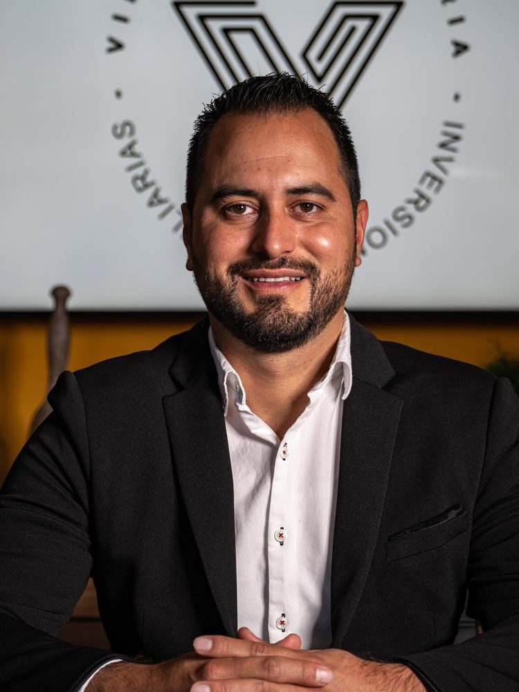 Luis López con saco negro y camisa blanca, sentado frente al logotipo de Vibien Inmobiliaria